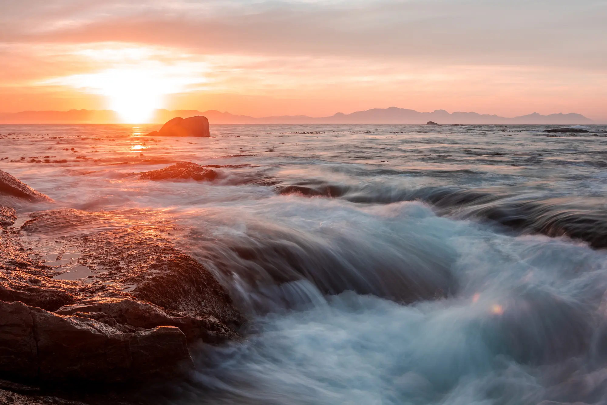 Water surging over rocks at sunrise against a burning orange horizon