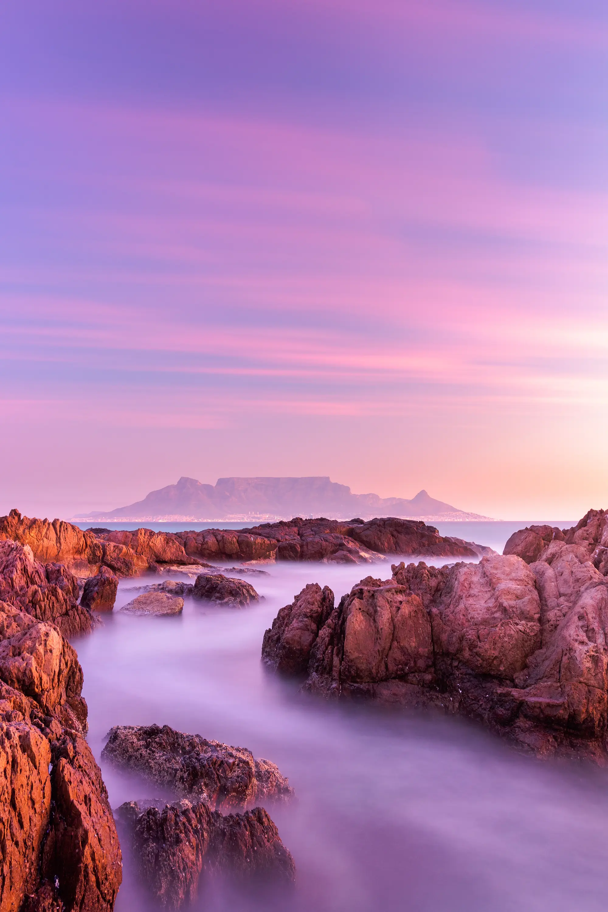 Table Mountain at sunset from the Blouberg S-bend, the sea reduced to purple mist between warm-toned rocks