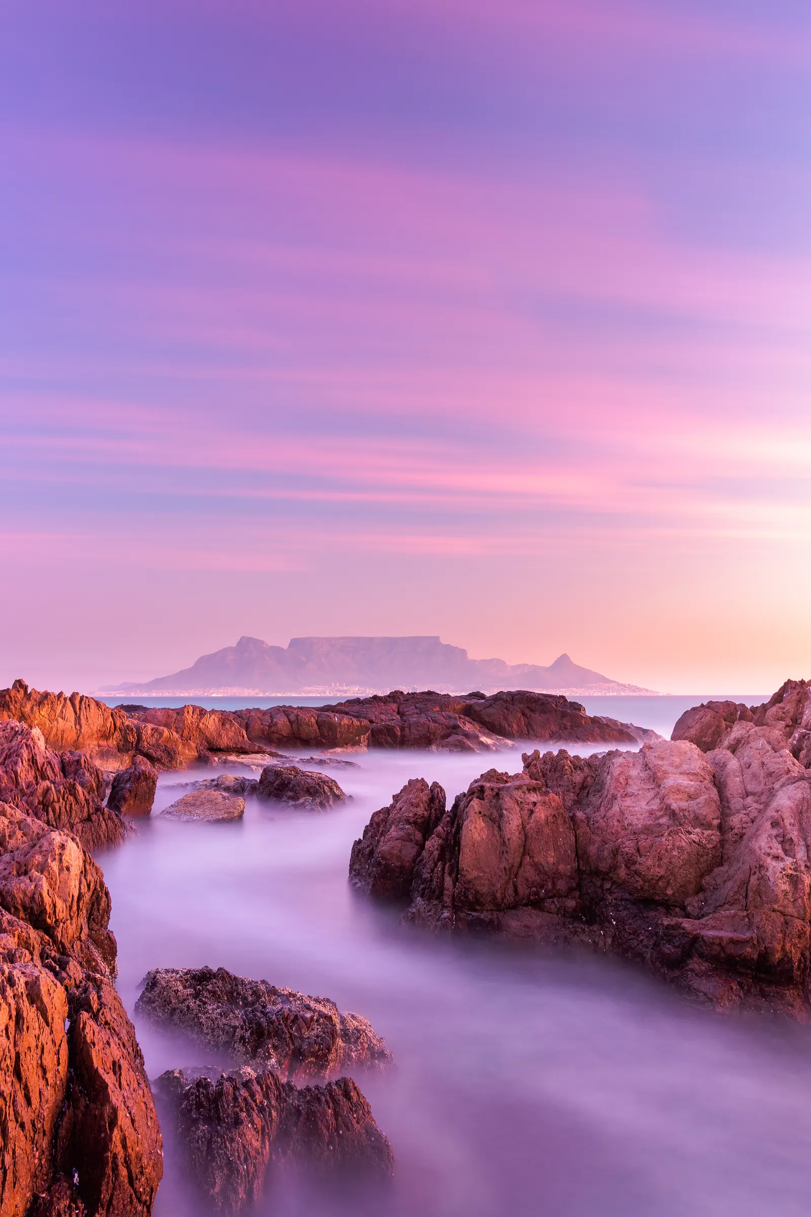 Table Mountain at sunset from the Blouberg S-bend, the sea reduced to purple mist between warm-toned rocks