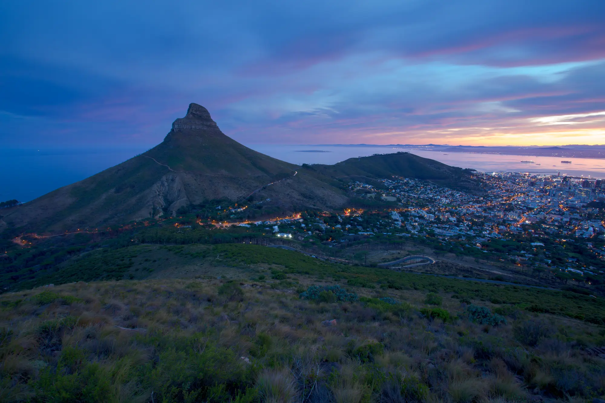 Lion's Head rising against a pre-dawn sky with Cape Town glowing amber below and the bay beyond